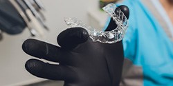 Dentist with black gloves holding clear aligner