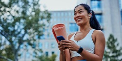 Smiling woman with yoga mat walking in park
